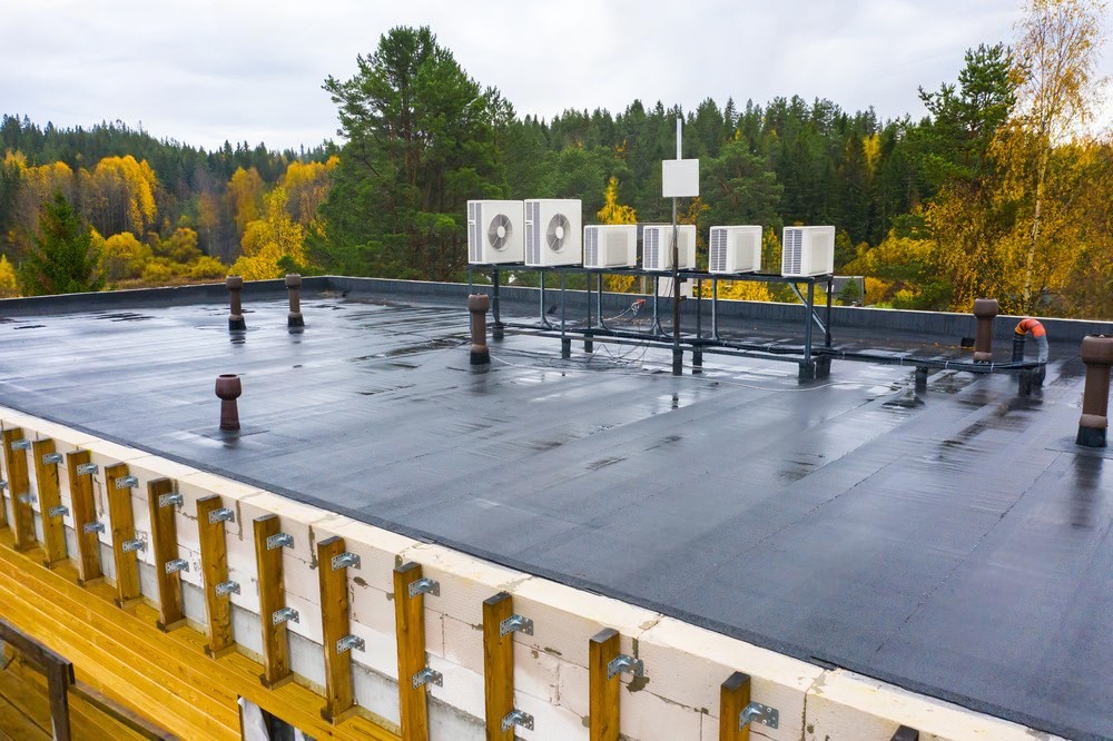 EPDM commercial flat roof with HVAC units and ventilation pipes in forested setting