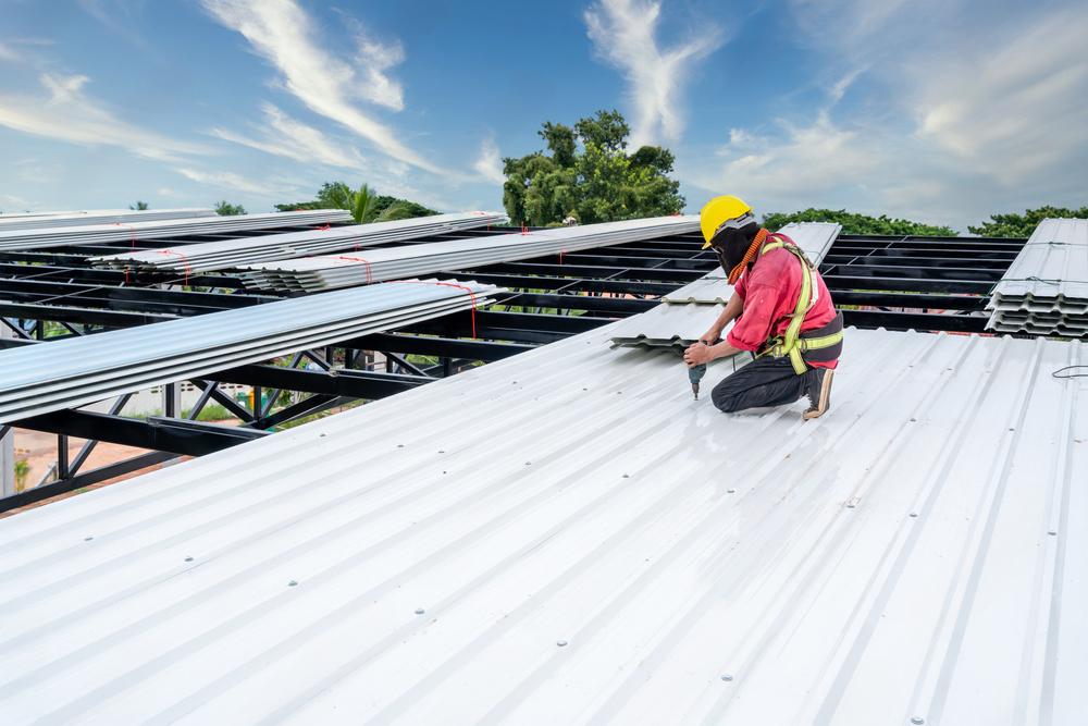 Roofing contractor installing white metal roofing panels on commercial building